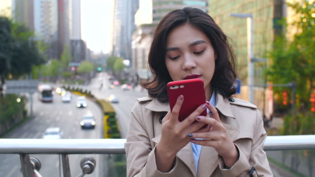 Bastante-feliz-joven-mujer-asiática-mediante-teléfono-móvil-en-la-ciudad-China-de-Chengdu,-en-la-tarde-en-el-puente-con-la-carretera-muy-transitada-en-el-fondo