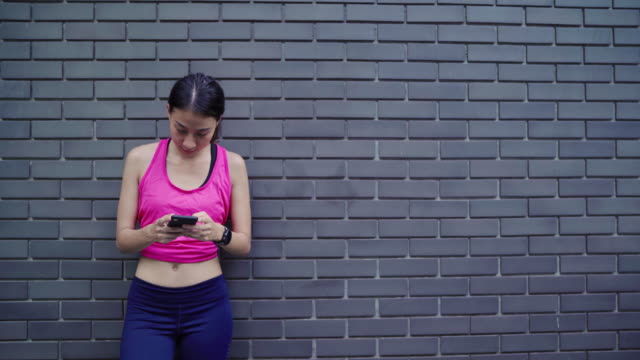 Gesunde-schöne-junge-asiatische-Sportler-Frau-mit-Smartphone-für-die-sozialen-Medien-während-der-Überprüfung-nach-dem-Ausführen-in-der-Großstadt-entspannen.-Lifestyle-Frauen-trainieren-in-der-City-Konzept.