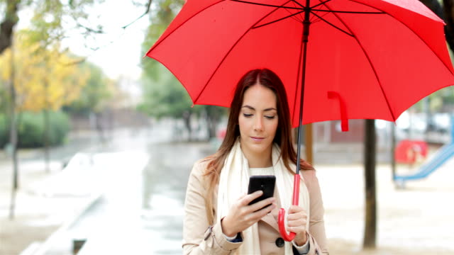 Serious-woman-checking-phone-under-the-rain
