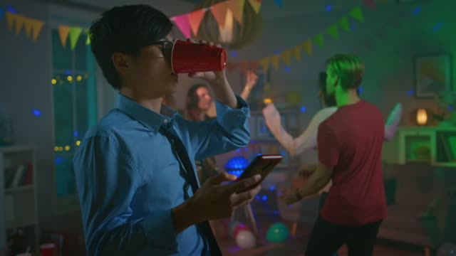 En-la-fiesta-salvaje-de-la-casa:-hombre-asiático-de-confianza-usa-Smartphone-en-vez-de-bailar-con-otras-personas.