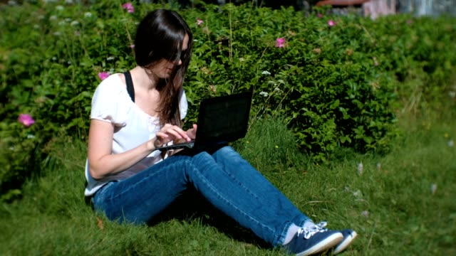 Hermosa-morena-niña-escribiendo-en-la-computadora-portátil-sentado-en-el-parque-en-verano.