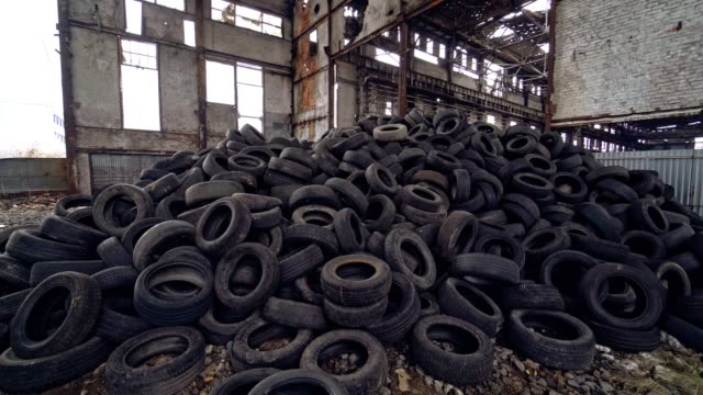 Pila-de-neumáticos-usados-del-coche-están-en-el-suelo-dentro-de-una-fábrica-abandonada-en-el-fondo-de-las-viejas-paredes-grises