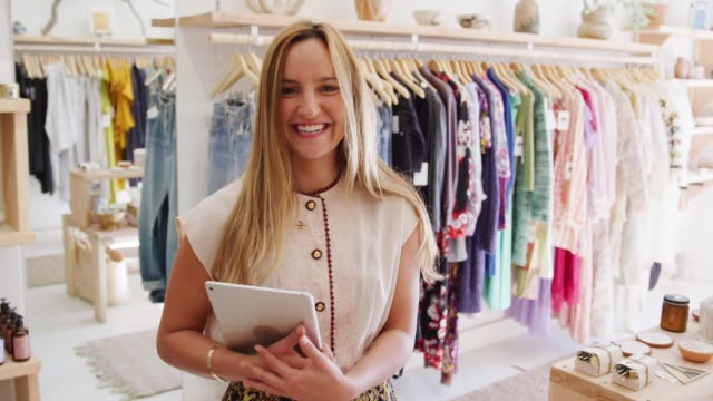 Female-owner-of-independent-clothing-store-with-digital-tablet-smiling-at-camera---shot-in-slow-motion