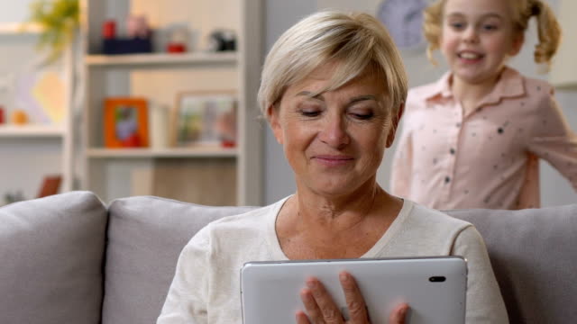 Granny-comprobando-vacaciones-aplicación-en-la-tableta,-celebrando-el-cumpleaños-con-la-nieta