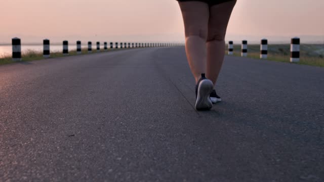Übergewichtige-asiatische-Frauen-joggen-am-frühen-Morgen-im-Sonnenlicht-auf-der-Straße.-Konzept-des-Gewichtsverlustes-mit-Bewegung-für-die-Gesundheit.-Langsame-Bewegung,-Bottom-Ansicht