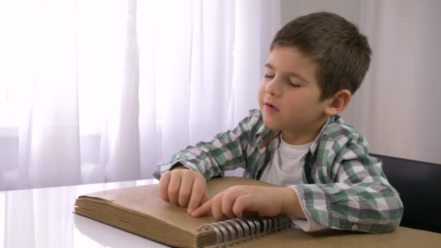 Lernen-für-blinde,-kranke-Junge,-die-Braille-Buch-mit-Zeichen-Schriftart-für-Sehbehinderte-am-Tisch-sitzen