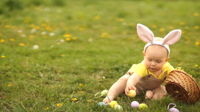 Lovely-baby-in-an-Easter-bunny-costume-collects-Easter-eggs-in-a-basket-sitting-on-the-grass-in-the-park.-Spring-picnic,-happy-easter-family