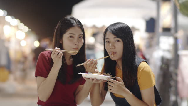 Asiatische-junge-Frauen-Freunde-reisen-in-Bangkok,-Thailand,-schöne-weibliche-Gefühl-glücklich-zu-Fuß-und-essen-Pad-Thai-in-der-Khao-San-Road.-Frauen-reisen-essen-Streetfood-Konzept.-Zeitlupenaufnahme.