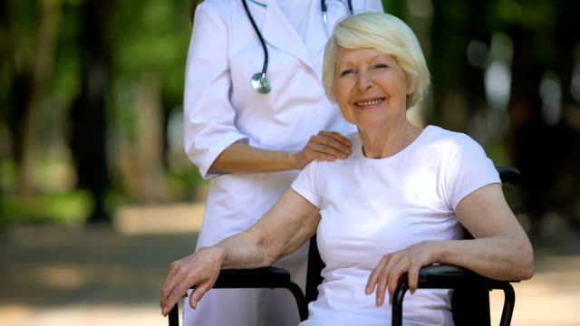 Doctor-putting-hand-on-shoulder-of-handicapped-elderly-woman-looking-at-camera