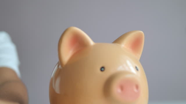 Close-up-hands-of-woman-putting-coin-into-the-piggy-bank-metaphor-saving-money-for-better-future-select-focus-shallow-depth-of-field