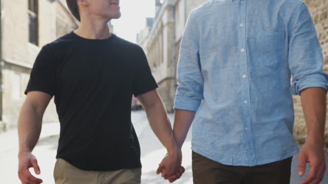 Liebende-männliche-Homosexuell-Paar-halten-Hände-zu-Fuß-entlang-der-City-Street