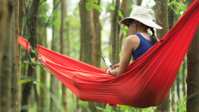 Woman-relaxing-in-hammock-with-smartphone-in-rainforest,4k