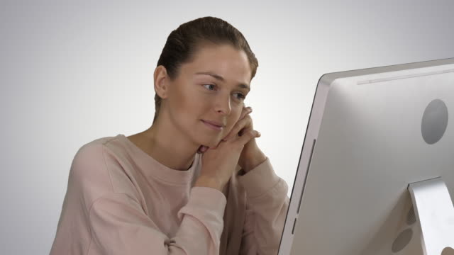 Blonde-girl-with-pink-pullover-looking-at-monitor-of-computer-watching-video-on-gradient-background