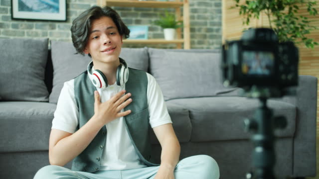 Cheerful-teenager-talking-gesturing-in-front-of-camera-recording-video-for-vlog