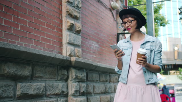 Slow-motion-of-smiling-girl-using-smartphone-holding-drink-walking-outdoors