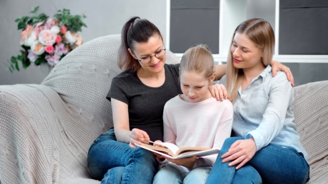 Two-happy-young-mother-reading-book-with-teenage-daughter-having-positive-emotion