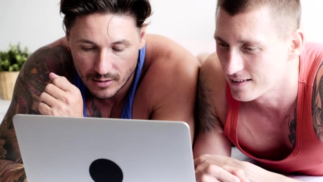 Gay-couple-in-bed-using-laptop-computer.-Focus-mood.