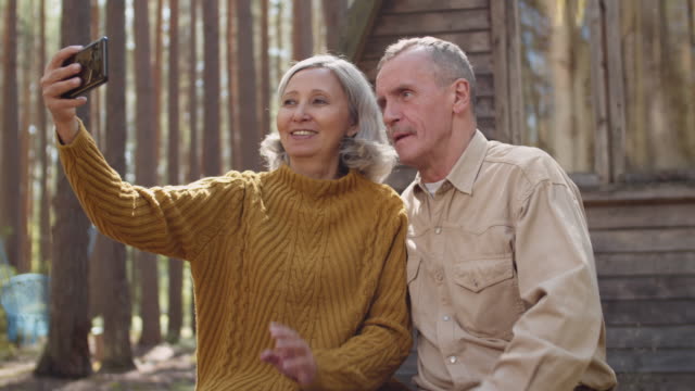 Old-Couple-Having-Video-Call-near-Wooden-House