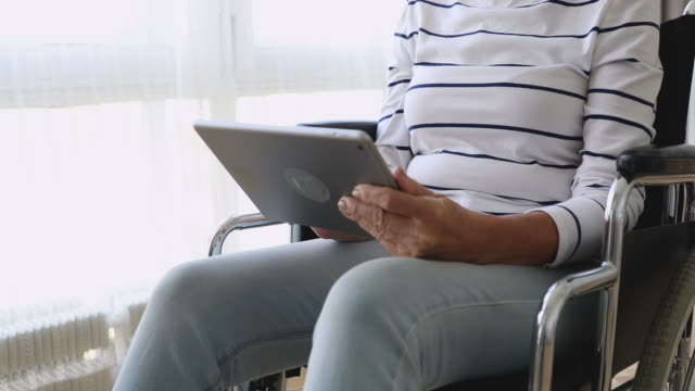 Anciana-discapacitada-se-sente-en-silla-de-ruedas-usando-tableta-digital,-primer-plano