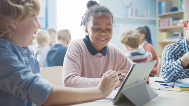 In-der-Grundschule:-Mädchen-und-jungen-Arbeiten-als-Team-mit-Tablet-Computer.-Vielfältiges-Klassenzimmer-mit-Kindern,-die-Programmiersprache-und-Softwaredesign-lernen