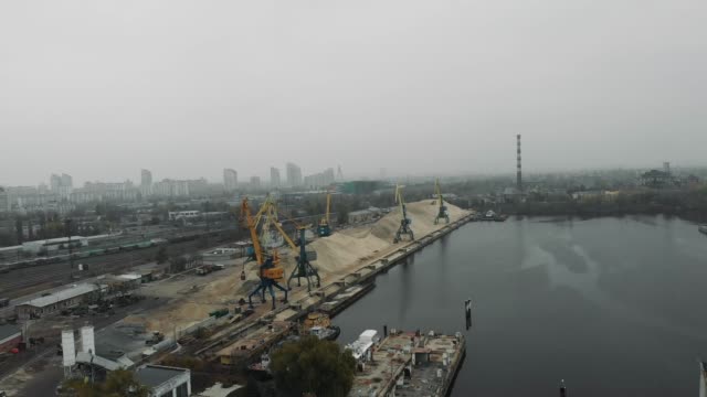 Baukräne-im-Industriepark-der-Stadt-bewegen-Sand-von-Binnenschiff-zu-Sand-Lkw.-Luftbild