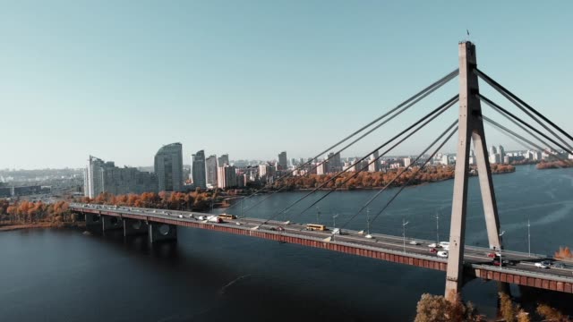 Concrete-bridge-with-cars-across-river-in-metropolis.-Drone-flying-near-big-city-bridge-with-high-rise-buildings-on-background.-Aerial-view-of-city-center-with-river-and-bridge.-Kyiv,-Ukraine