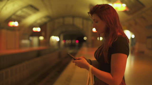 Attraktive-Rotschopf-Frau-mit-Sommersprossen,-Piercings-und-roten-Haaren-plaudern-auf-dem-Smartphone-an-der-U-Bahn-Station,-während-sonnigen-Sommer-in-Paris.-Verschwommener-unterirdischer-Hintergrund.-4K-UHD.