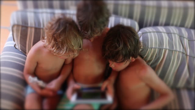 Ehrliche-Kinder-mit-Tablet-Bildschirm-Kinder-sitzen-auf-Sofa-Blick-auf-Tech-Gerät