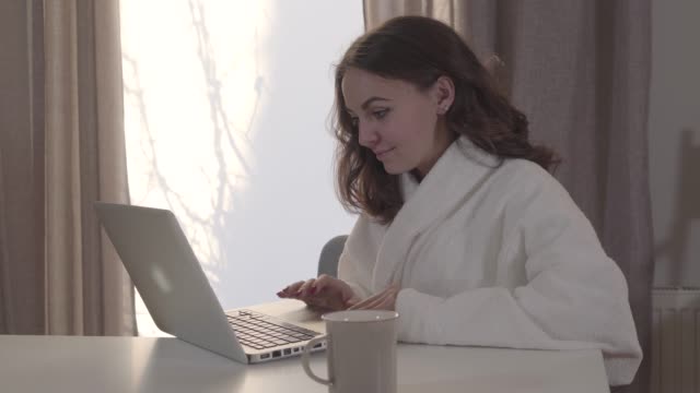 Portrait-of-young-pretty-Caucasian-girl-surfing-Internet-at-home.-Beautiful-brunette-woman-using-laptop-and-making-faces-as-looking-at-screen.-Internet,-online,-social-media.