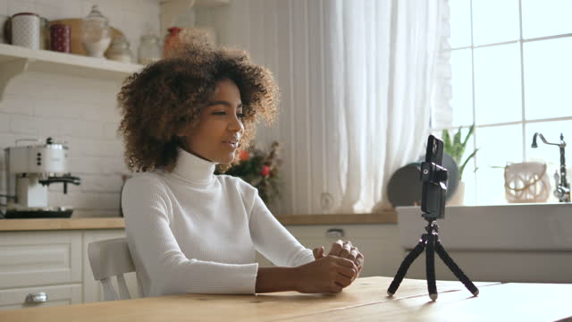 Happy-dark-skinned-lady-sits-at-table-and-shoots-video-blog