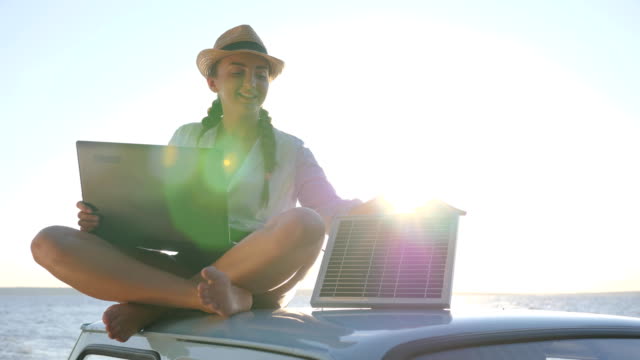 nueva-tecnología,-chica-feliz-se-sienta-en-el-coche-clásico-techo-con-batería-solar-y-portátil-en-las-manos-al-aire-libre,-mujer-sentada-en-el-coche