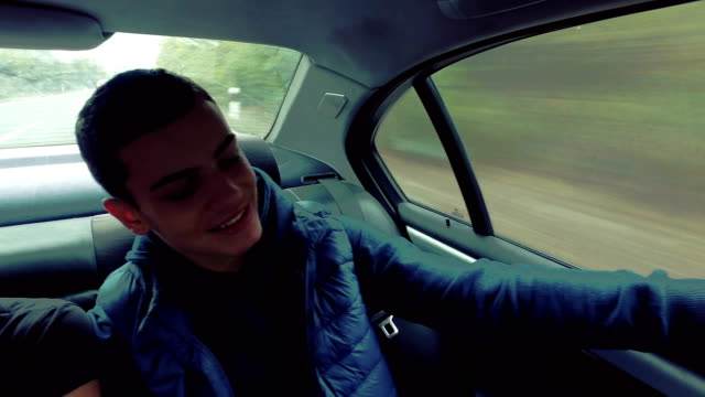 Happy-male-teen-takes-selfie-driving-on-backseat-on-luxury-car