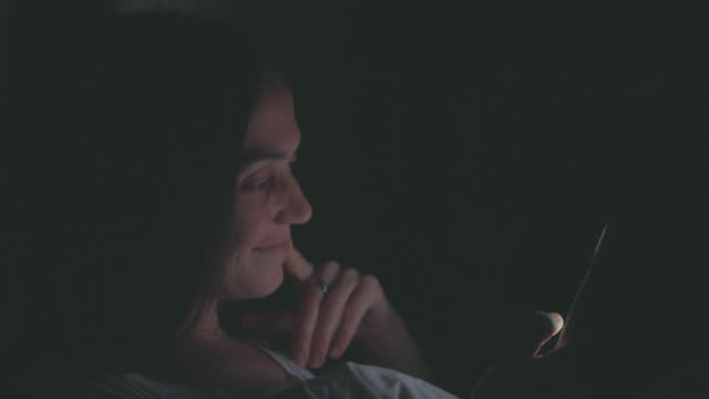 Young-woman-using-cellphone-on-bed-at-night