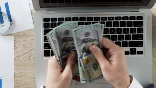 Empresario-contando-billetes-de-un-dólar-en-sus-manos,-poniéndolas-en-laptop,-renta