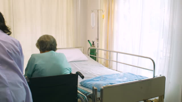 Professionelle-Ärztin-hilft-ihren-Patienten-vom-Rollstuhl-zum-Bett-im-Krankenhaus