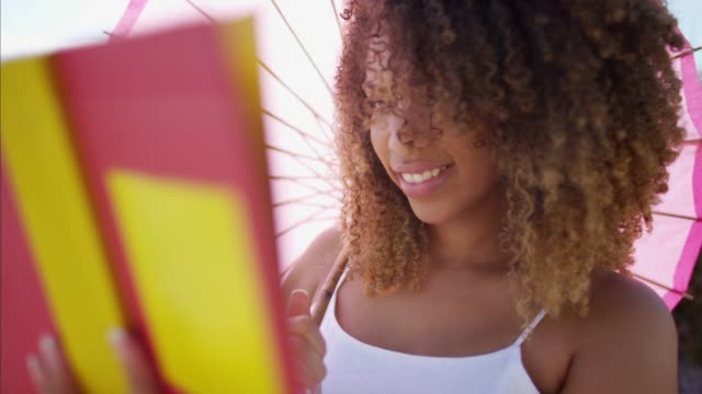 African-American-Frauen-lesen-unter-Sonnenschirm-am-Strand