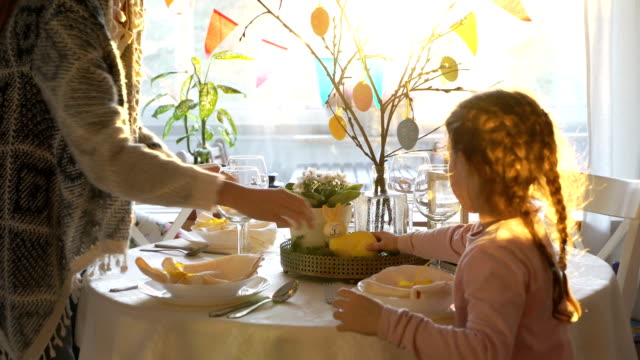 Mujer-y-su-hijita-están-estableciendo-mesa-festiva-de-Pascua-con-conejito-y-huevos-la-decoración