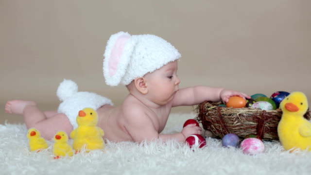 Niedlichen-kleinen-Kleinkind-Baby-jungen-spielen-mit-bunten-Ostereiern-und-kleinen-Zierenten,-isoliert-erschossen,-Beige-Hintergrund