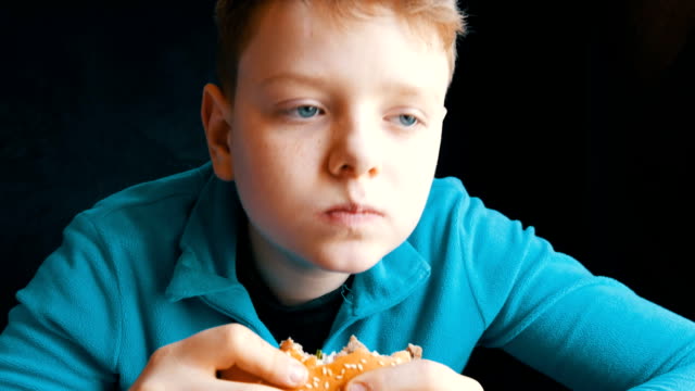 Mouth-of-a-teenager.-The-boy-with-an-appetite-eats-big-hamburger-in-a-fast-food-restaurant