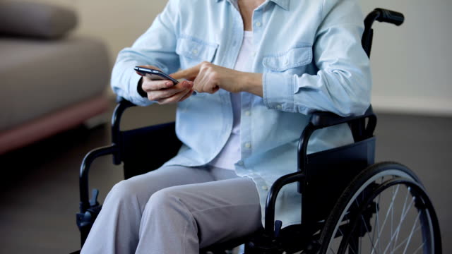 Female-pensioner-in-wheelchair-browsing-internet-on-smartphone,-communication