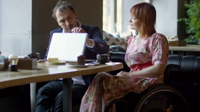 Frau-im-Rollstuhl-und-Mann-mit-Laptop-im-Café-plaudern