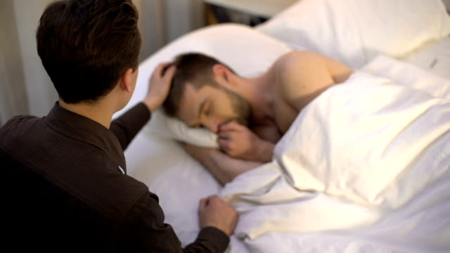 Young-man-stroking-sleeping-partner-head,-homosexual-couple,-tender-relations