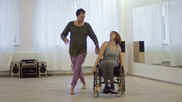Hombre-expresivo-bailando-con-mujer-parapléjico-en-silla-de-ruedas-en-estudio