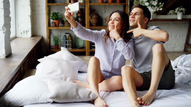 Hübsche-Asiatin-nimmt-Selfie-mit-ihren-hübschen-kaukasischen-Freund-holding-Smartphone-posiert-und-küssen.-Romantische-Beziehung-und-social-Media-Konzept.