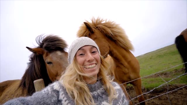Blondes-Haar-Mädchen-in-Island-unter-Selfie-Porträt-mit-Islandpferd-in-grüne-Wiese.-Im-Frühling,-Bewölkter-Himmel,-Frau-trägt-isländischen-grau-wolle-Pullover-gedreht.-Die-Leute-reisen-tierischen-Zuneigung-Konzept-Zeitlupe