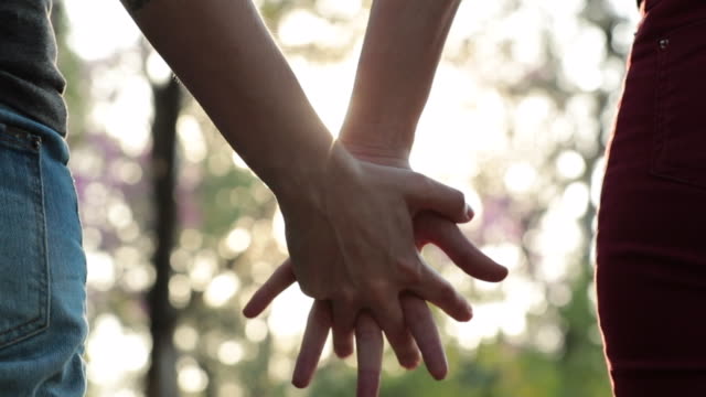 Close-up-of-couple-holding-hands-together-at-the-park-with-sunlight-flare-in-the-background