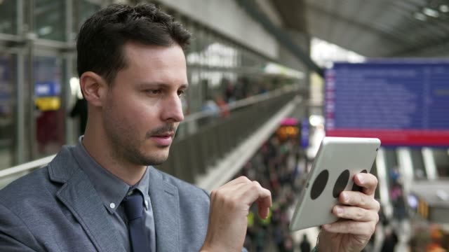 Handsome-young-businessman-writing-texts-on-digital-tablet-in-public-space