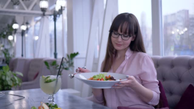 gesunder-Lebensstil,-Mädchen-mit-langen-Haaren-in-Brillen-mit-einer-Gabel-und-Teller-in-der-hand-griechischen-Salat-essen-und-Blick-in-die-Kamera