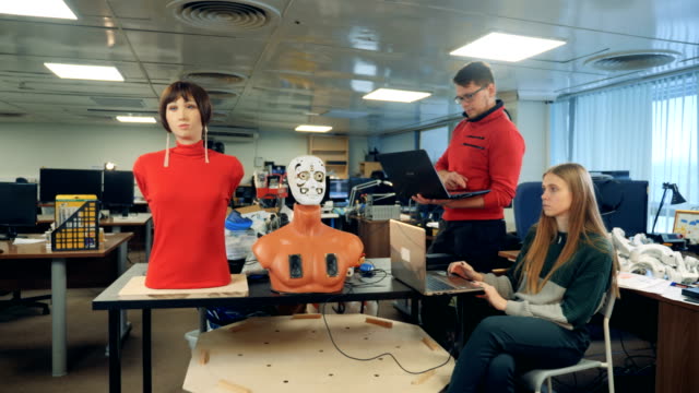 Hombre-y-mujer-controlar-un-robot,-utilizando-ordenadores-portátiles,-cerca.
