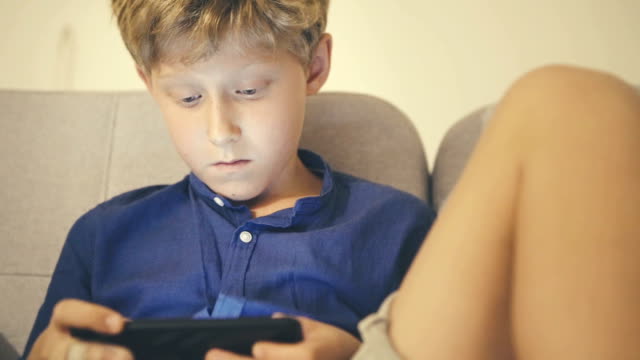 Niño-sentado-en-el-sofá-sosteniendo-el-teléfono-inteligente-en-las-manos-jugando-juego